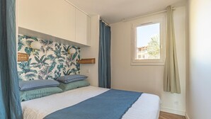 Un dormitorio con cama, cabecera decorada con arte en la pared, ventana con cortinas y vista a edificios.