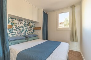 A bedroom with a bed, a headboard with wall art, a window with curtains, and a view of buildings outside.