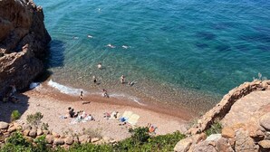 Una playa rocosa con aguas cristalinas, gente nadando y tomadores de sol.