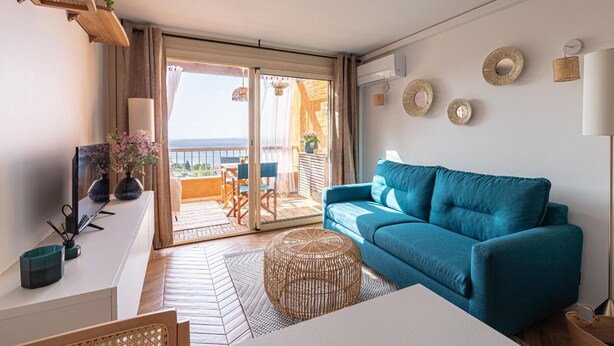 Una sala moderna con un sofá azul, una mesa de centro de mimbre y un ventanal con vistas al exterior.