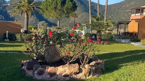 Un jardín con flores rojas, palmeras y una montaña al fondo.
