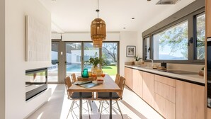 A modern kitchen with a dining area, large windows, and a view of the outdoors.