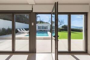 Ein modernes Haus mit Pool, Schiebetüren und Blick auf eine grüne Rasenfläche.