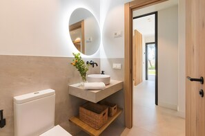 A modern bathroom with a toilet, a sink with a mirror, wicker baskets, and a wooden door. - Villa 'Casa Rural Acogedora Y Con Estilo' with Mountain View, Wi-Fi and Air Conditioning (Málaga)