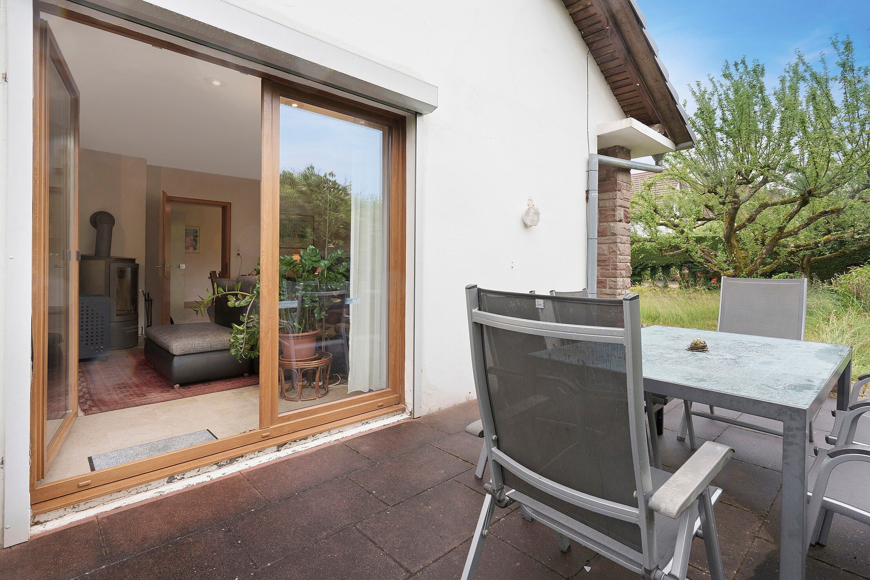A patio with a table and chairs, a sliding glass door leading to an interior room, and a tree in the background.