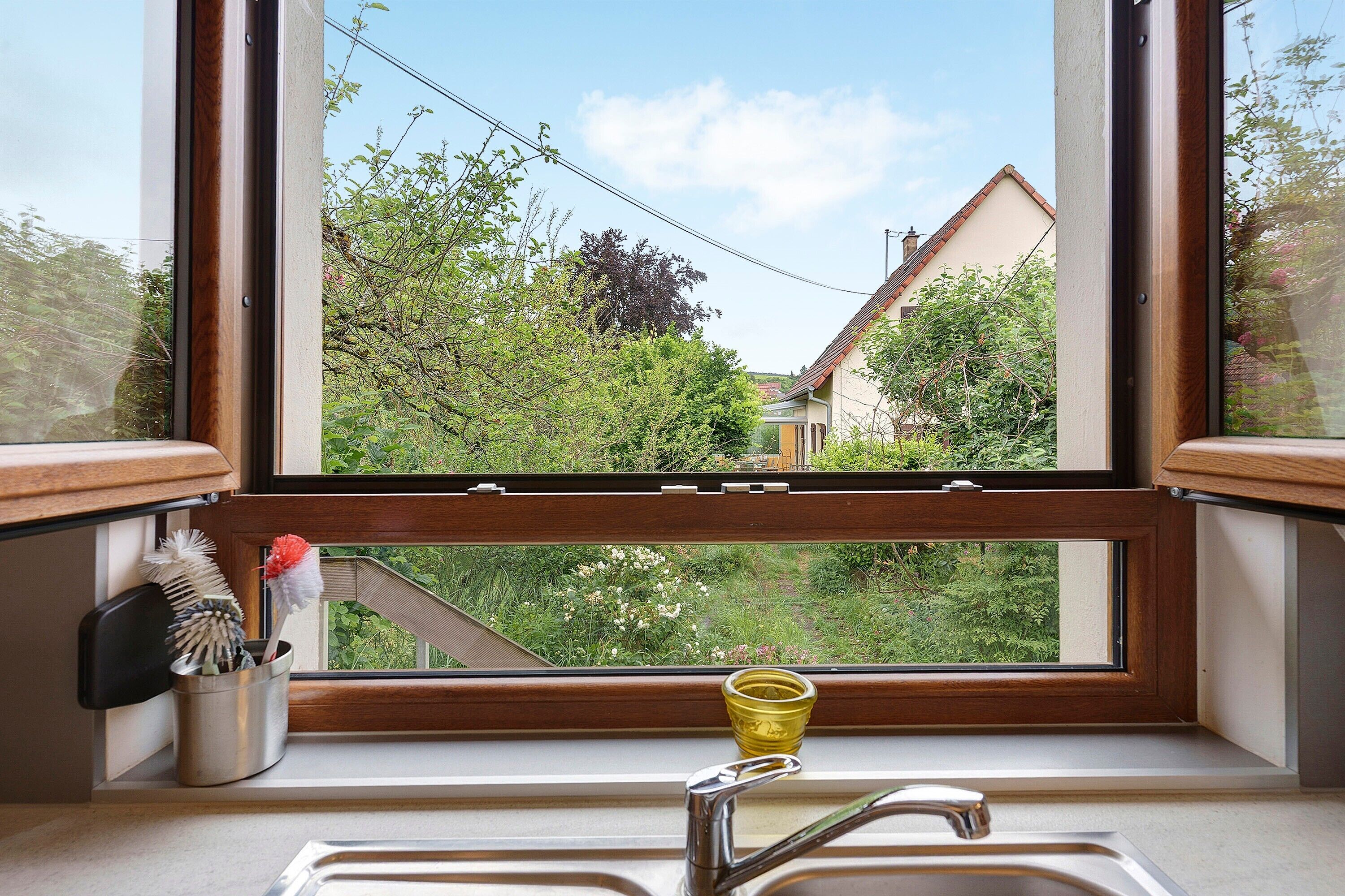 A kitchen with a window, a sink, and a metal container with brushes.