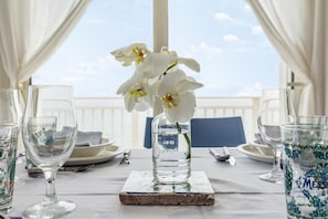 Une table dressée avec de beaux verres, un vase rempli de fleurs blanches et une vue sur le ciel par la fenêtre.