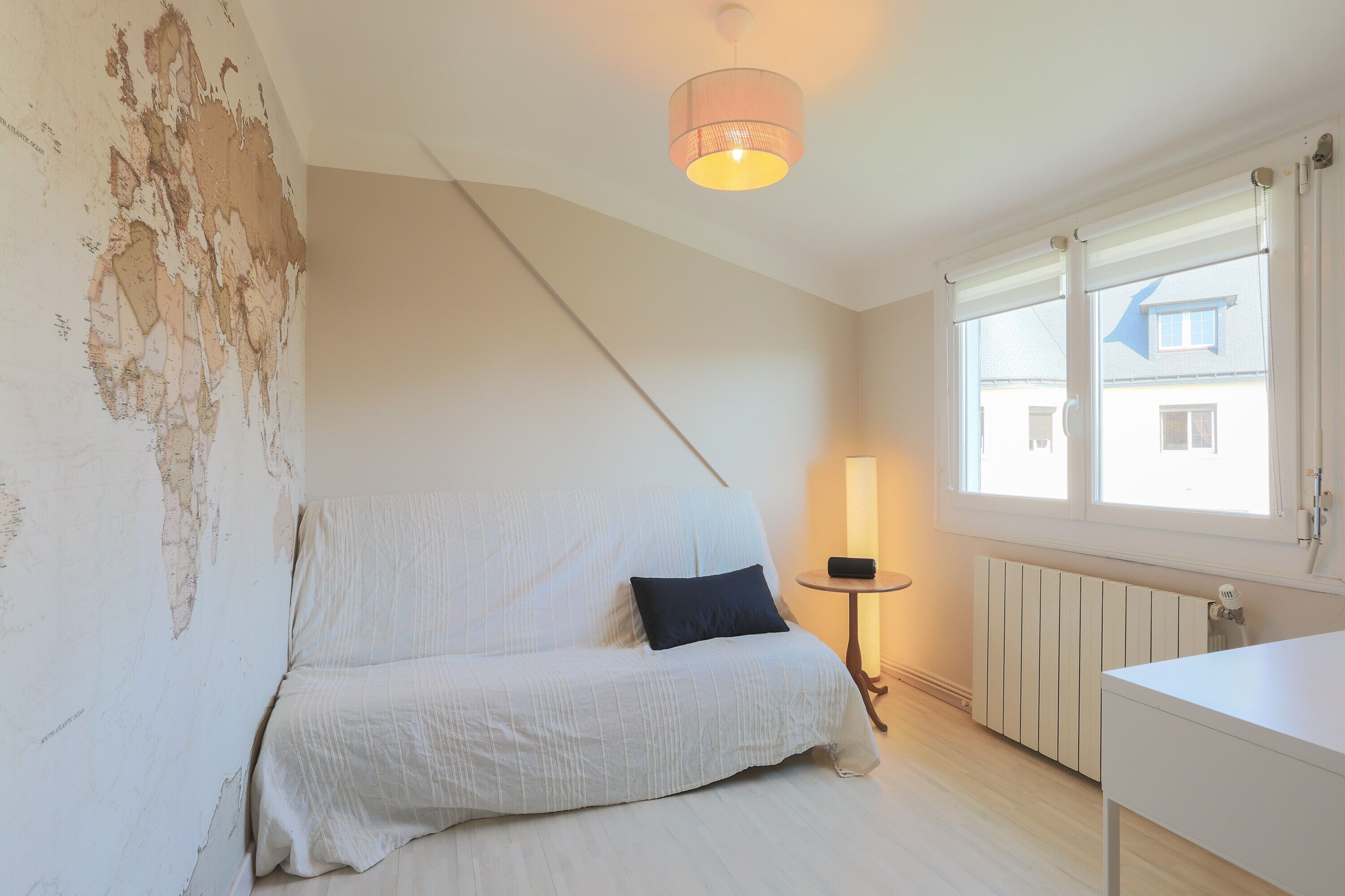 Una habitación con una cama blanca, una lámpara de noche, un radiador y una ventana con persianas.