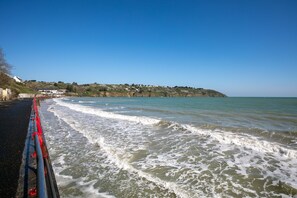 A coastal road with a railing, waves, and a distant hillside with buildings. - Holiday Home 'Charmante Maison' with Private Garden and Wi-Fi (Plérin)