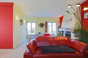 Un salon avec un canapé en cuir rouge, un coin repas avec une table et des chaises, et une cuisine équipée d’une cuisinière et de placards.