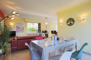 Un espace repas comprenant une table, des chaises et un canapé. Des lampes murales et une affiche ornent le mur.
