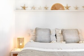 A neatly arranged bedroom with a bed, pillows, a bedside lamp, and decorative starfish on a shelf.