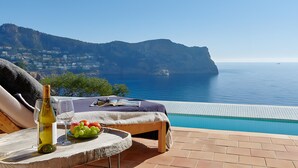 A poolside lounge with a view of the sea and mountains, a bottle of wine, and a plate of fruit. - Villa 'Mallorquin Oasis' with Sea View, Wi-Fi and Air Conditioning (Andratx)