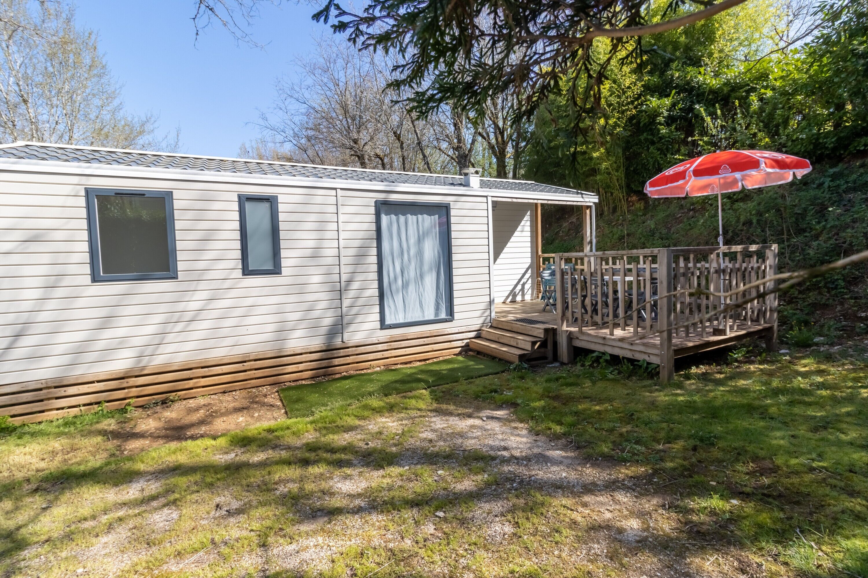 A mobile home with a deck, a red umbrella, and a wooden fence.