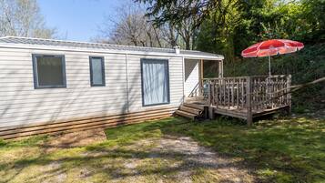 A mobile home with a deck, a red umbrella, and a wooden fence.