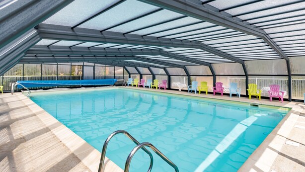 En indendørs swimmingpool med et glastag, omgivet af farverige stole.