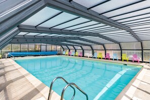 Une piscine intérieure dotée d’un toit en verre, entourée de chaises aux couleurs vives.