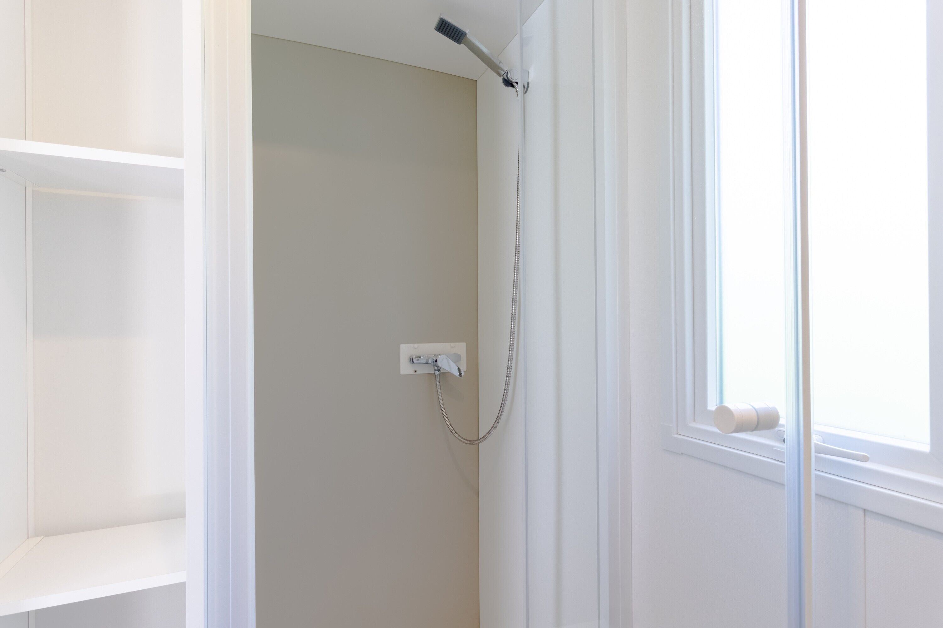 Un baño con ducha, ventana y puerta blanca.