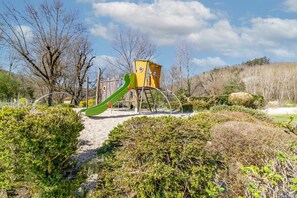 Un terrain de jeux avec un toboggan et des structures d’escalade, entouré d’arbustes et d’arbres.