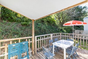 Une terrasse extérieure couverte, dotée d’une table et de chaises, entourée d’une terrasse en bois et d’une clôture en bois.