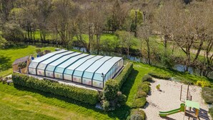 A large greenhouse structure with a glass roof, surrounded by well-maintained grass and trees, near a body of water. - Mobile Home "Calvi": Holidays in Dordogne, Shared Pool & Mini-Farm near Sarlat (Bouzic)