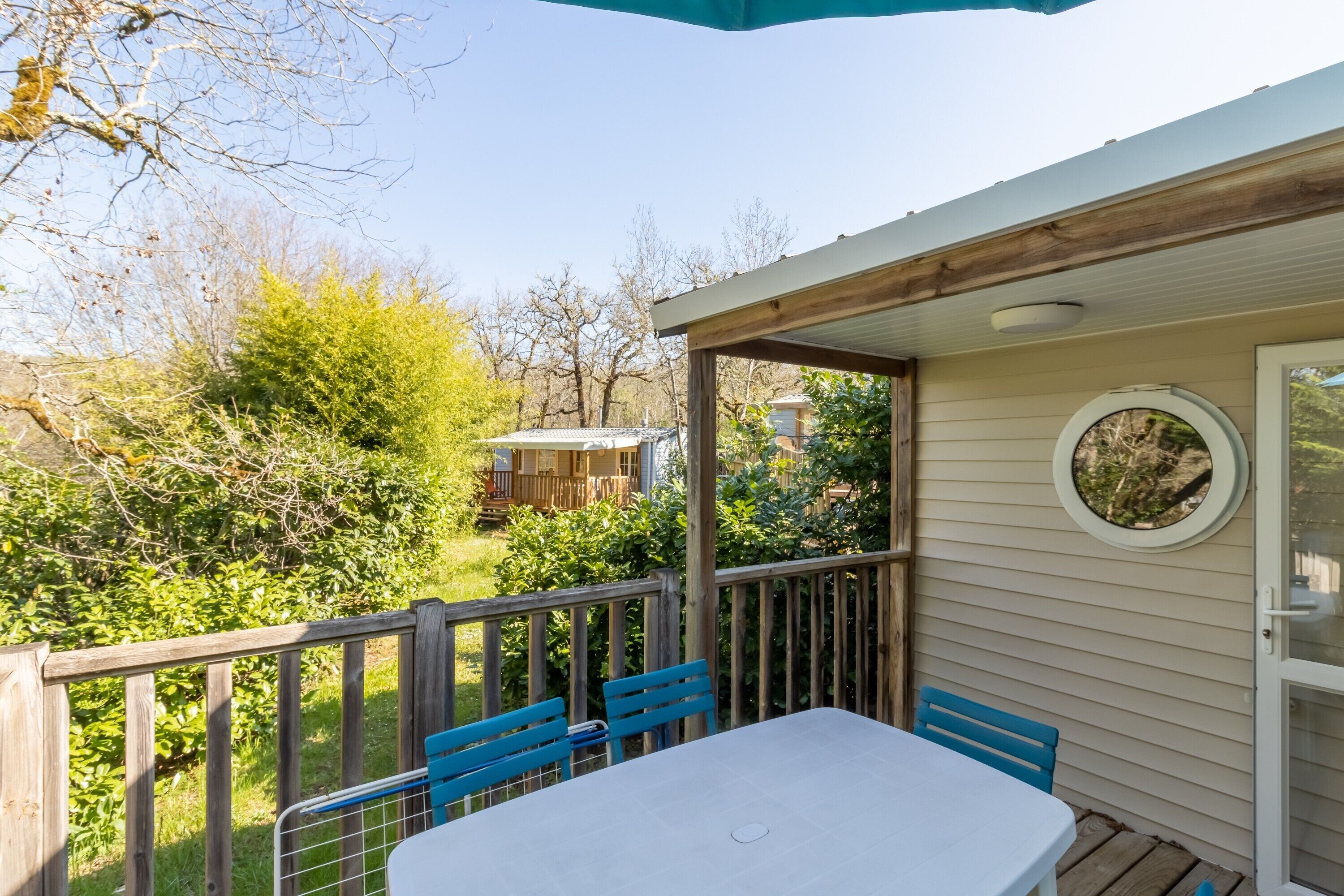 Eine überdachte Terrasse mit Tisch und Stühlen, eine Holzterrasse und Blick auf ein Haus und einen Garten.