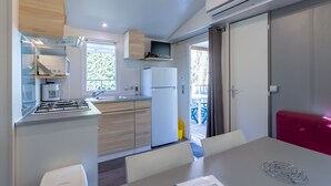 A compact kitchen with a gas stove, a refrigerator, and a microwave. There is a dining area with a table and chairs. - Mobile Home O'Hara 834T – Family Getaway: Shared Pools & Near Sarlat (Bouzic)