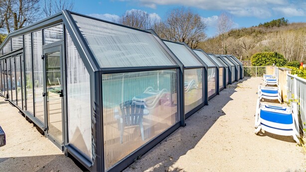 A row of glass-enclosed structures with a metal frame, each with a door and a window, and a gravel path leading to them. - Mobile Home O'Hara 834T – Family Getaway: Shared Pools & Near Sarlat (Bouzic)