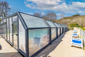 A row of glass-enclosed structures with a metal frame, each with a door and a window, and a gravel path leading to them.
