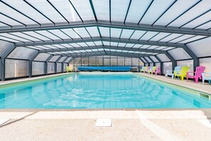 Une piscine dotée d’un toit en verre, entourée de chaises aux couleurs vives.