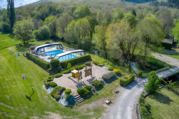 An aerial view of a property with a swimming pool, a tennis court, and a well-maintained garden.