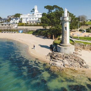 Un paysage côtier avec un phare, une plage et un grand bâtiment blanc surmonté d’une tour.