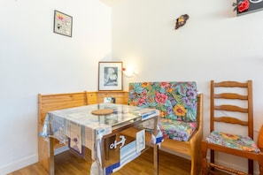 A small room with a wooden bed, a glass-top table with a quilt, a floral chair, and a wooden chair. - Studio Apartment 'Turquoise À 100m De La Plage' (Bénodet)