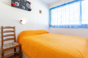A room with a bed, a chair, a wall-mounted light, and a window with blue curtains. - Studio Apartment 'Turquoise À 100m De La Plage' (Bénodet)