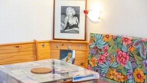 Una habitación con un armario de madera, un cuadro en la pared, un sofá floral y una mesa con superficie de vidrio.