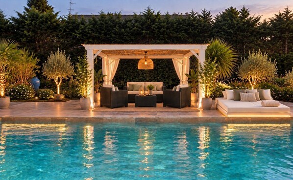 A poolside area with a covered seating area, lounge chairs, and a sofa.