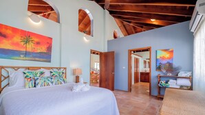 Un dormitorio con una cama, un cuadro de un atardecer, un espejo y vistas al baño.