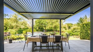 An outdoor patio with a covered dining area, a pool, and surrounding greenery. - Kerwall – Family Rooms with Shared Pool, Private Terrace, and Wi-Fi (Malville)
