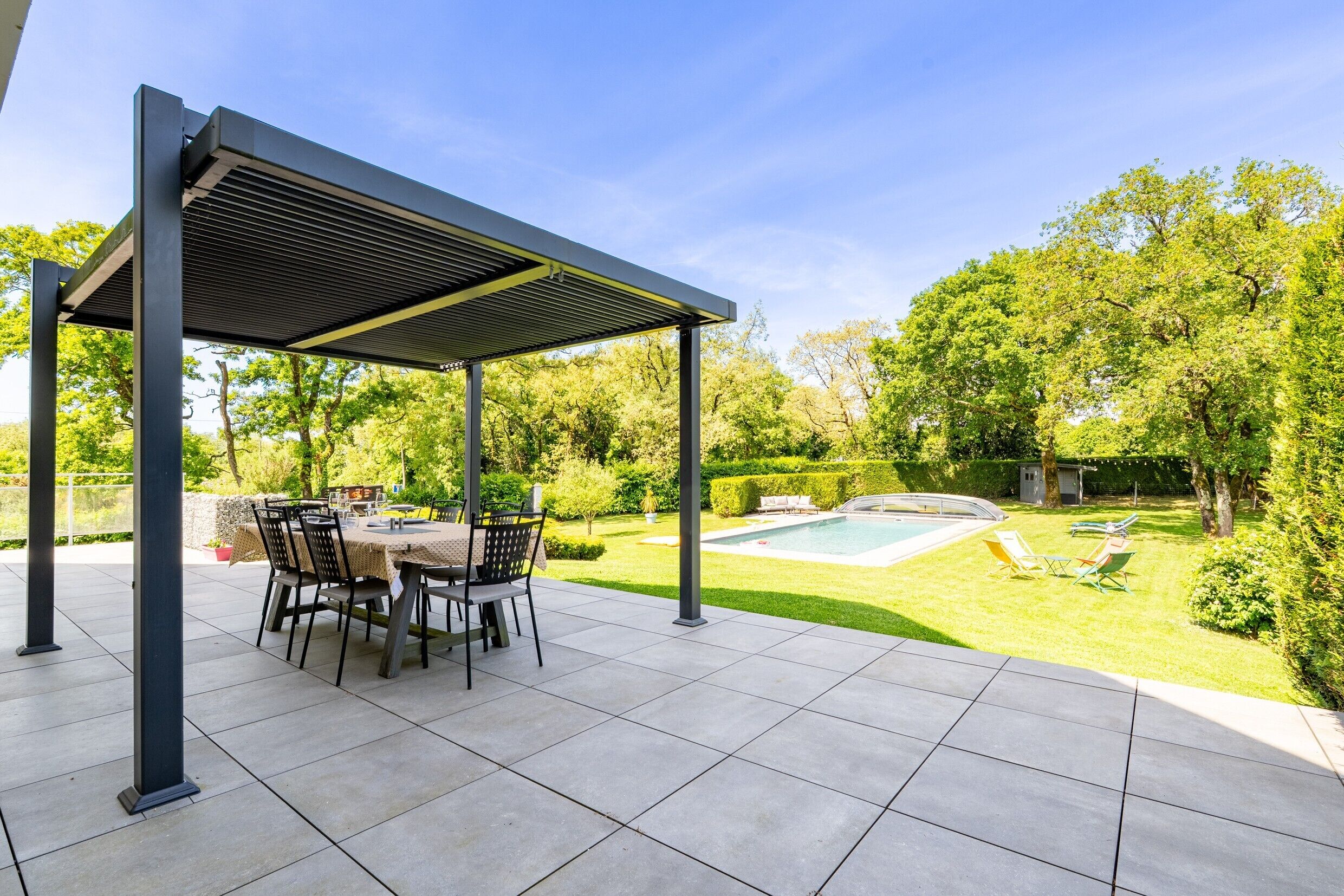 Un patio exterior con una mesa y sillas cubiertas, una piscina y un césped bien cuidado.