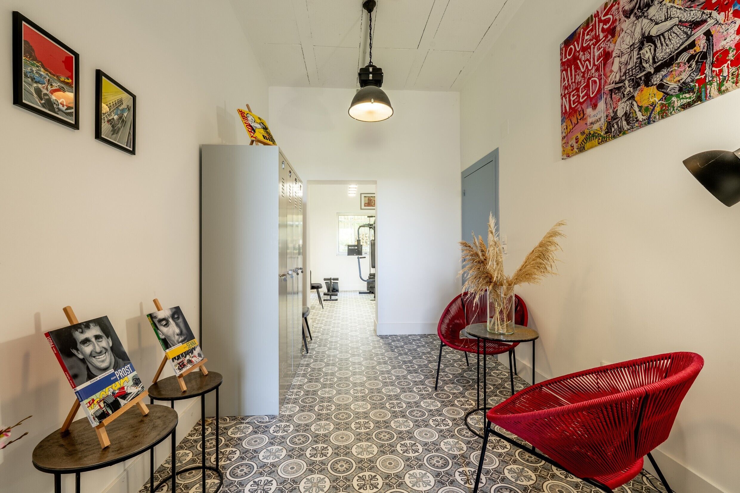 Un couloir avec un sol à motifs, une chaise rouge et des œuvres d’art encadrées accrochées aux murs.