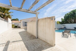 Un espace extérieur abrité comprenant une piscine, une pergola et une terrasse avec des chaises.