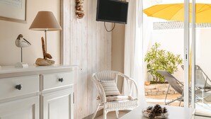 Ein Zimmer mit einem weißen Korbstuhl, einem Flachbildfernseher, einer Lampe und einem Esstisch mit einer Kiefernzapfen-Dekoration.