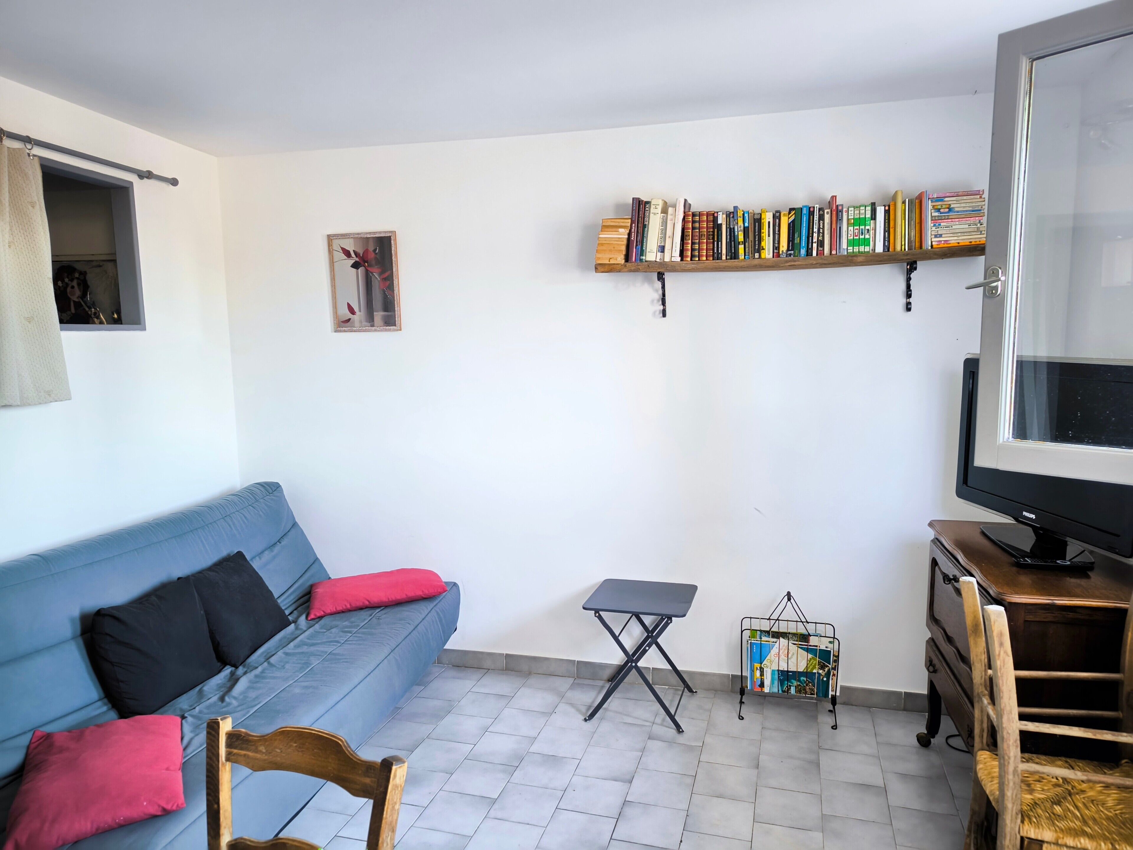 A living room with a blue sofa, a small table, a bookshelf, a TV, and a chair.