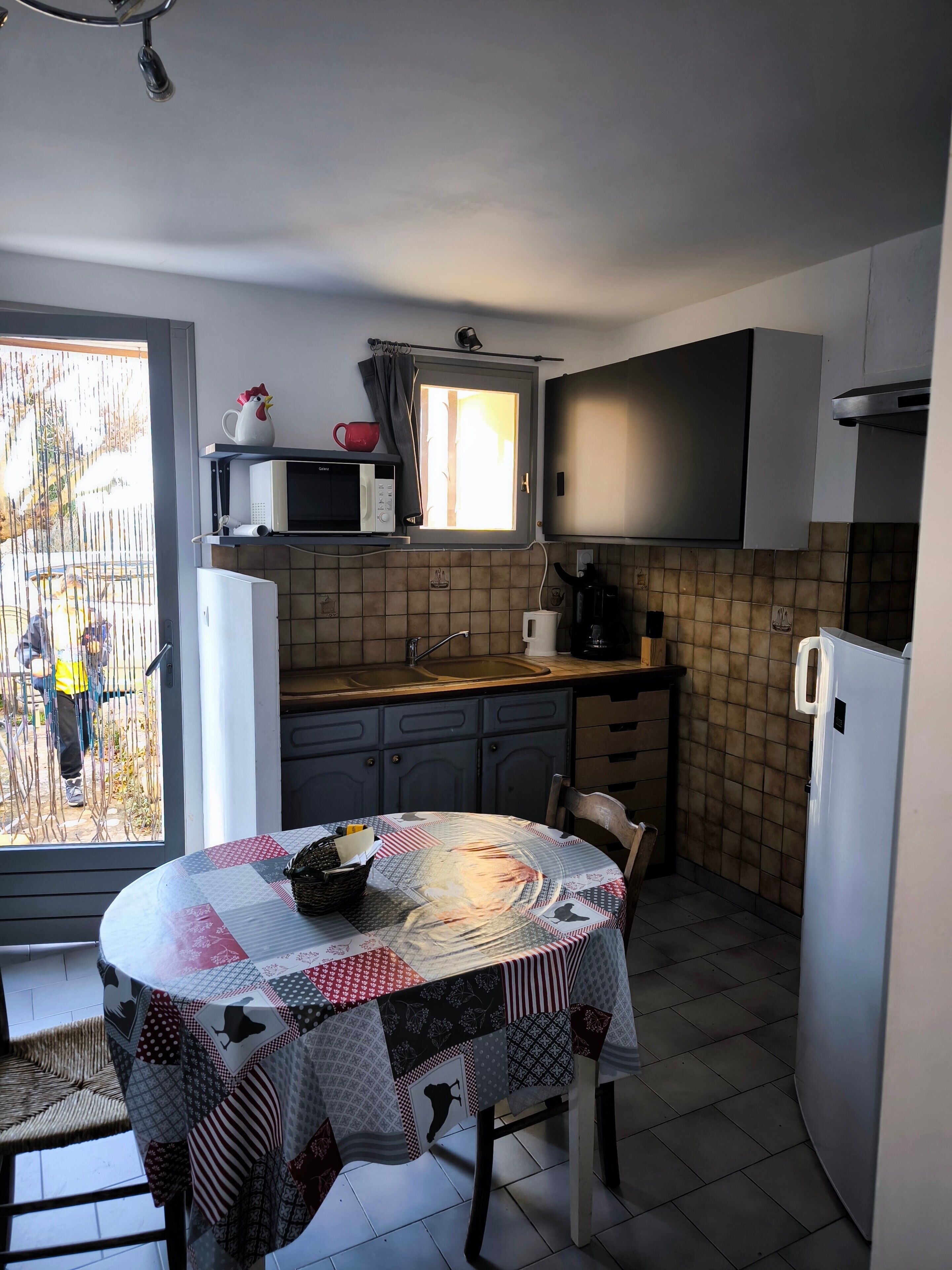 Een kleine keuken met een eettafel, een magnetron, een koelkast en kastjes.