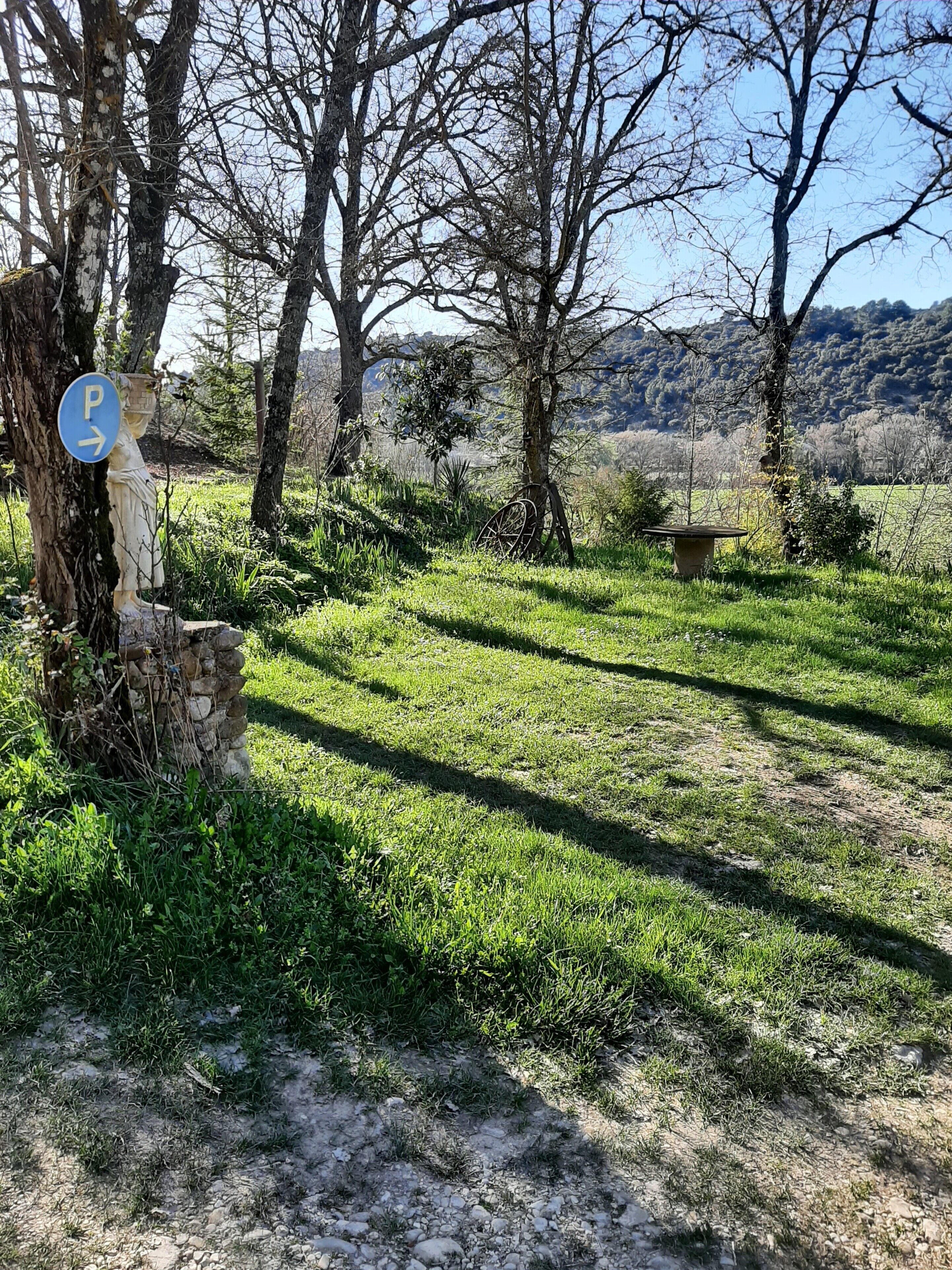 A rural landscape with a stone wall, a statue, and a sign indicating a parking area.