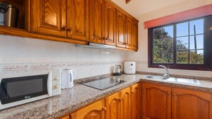 Une cuisine dotée de meubles en bois, d’un plan de travail en granit, d’un four à micro-ondes, d’une bouilloire, d’une machine à café et d’une fenêtre donnant sur les arbres.