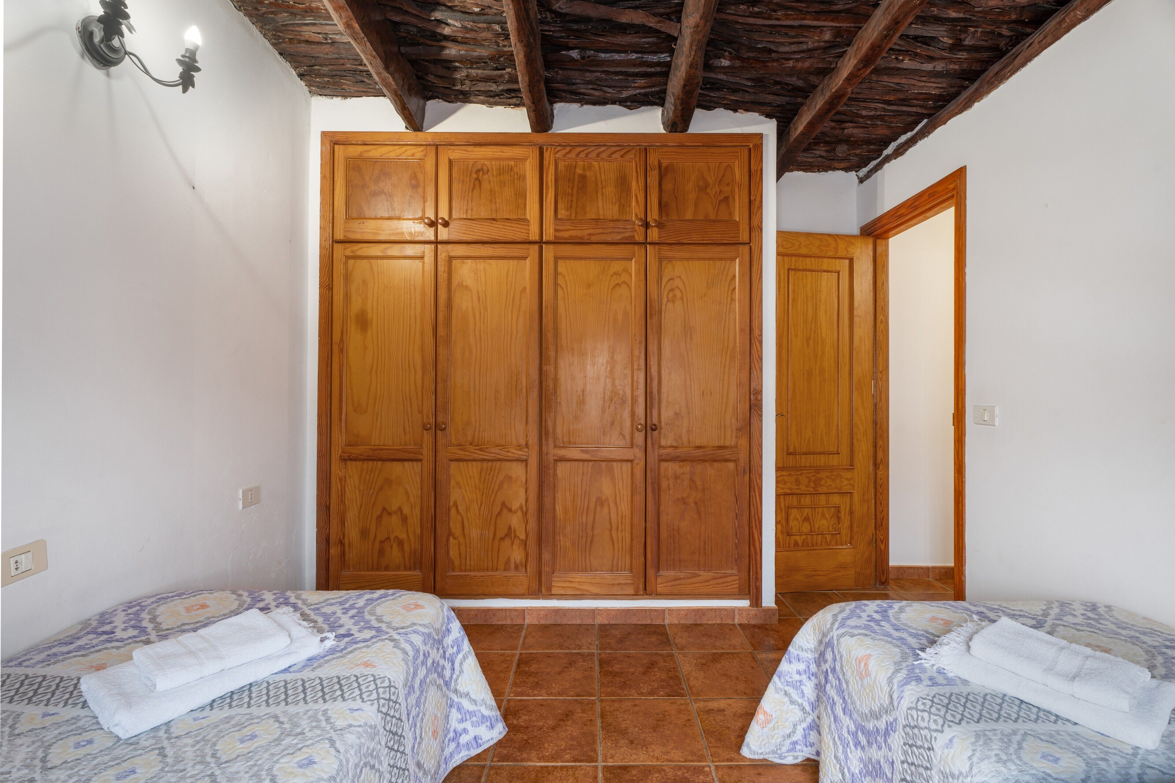 Een slaapkamer met twee bedden, een houten garderobe, betegelde vloer en een rustiek plafond.