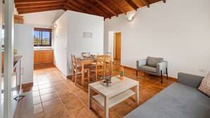 Un vaste espace de vie doté d’un plafond en bois, d’une table à manger avec des chaises, d’un canapé et d’une petite table sur laquelle est posée une plante en pot.