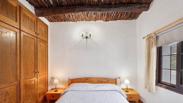 Une chambre à coucher avec une tête de lit en bois, deux tables de chevet avec des lampes, une grande armoire et une fenêtre avec des rideaux.