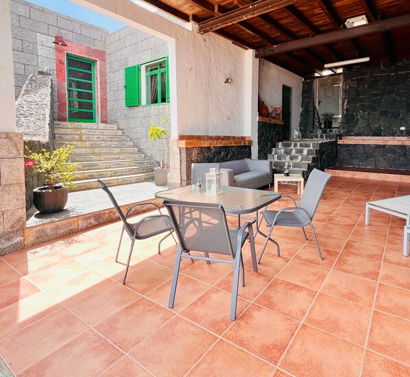 An outdoor patio with a table and chairs, a stone wall, and a staircase leading to a green door.